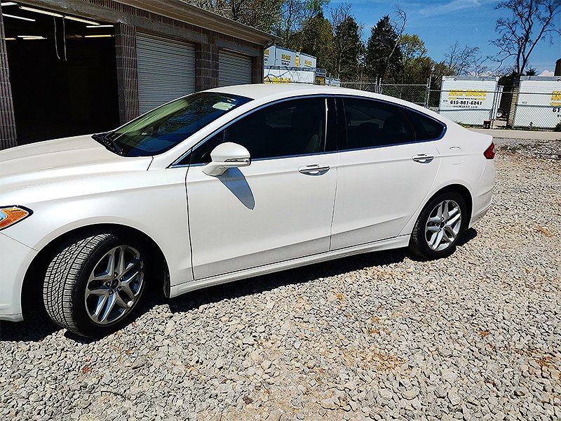 White sedan parked on gravel, near a building with garages, and a blue sky.