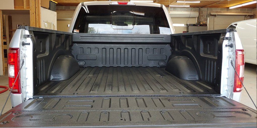 Open black bed of a silver pickup truck in a garage, with the tailgate down and the bed's interior visible.