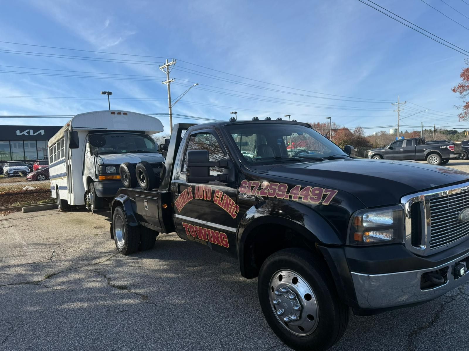 Tow truck towing a white bus on a sunny day. Black truck with business logo.