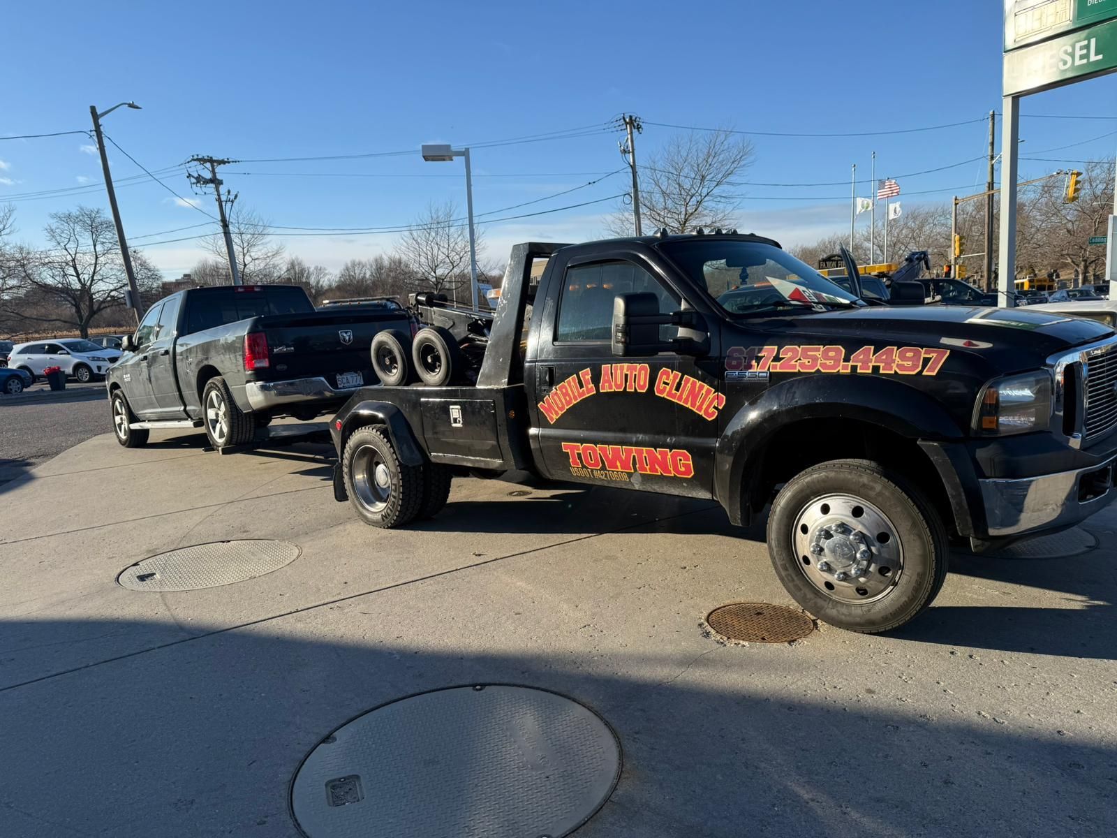 Black tow truck towing a black pickup truck on a sunny day. 