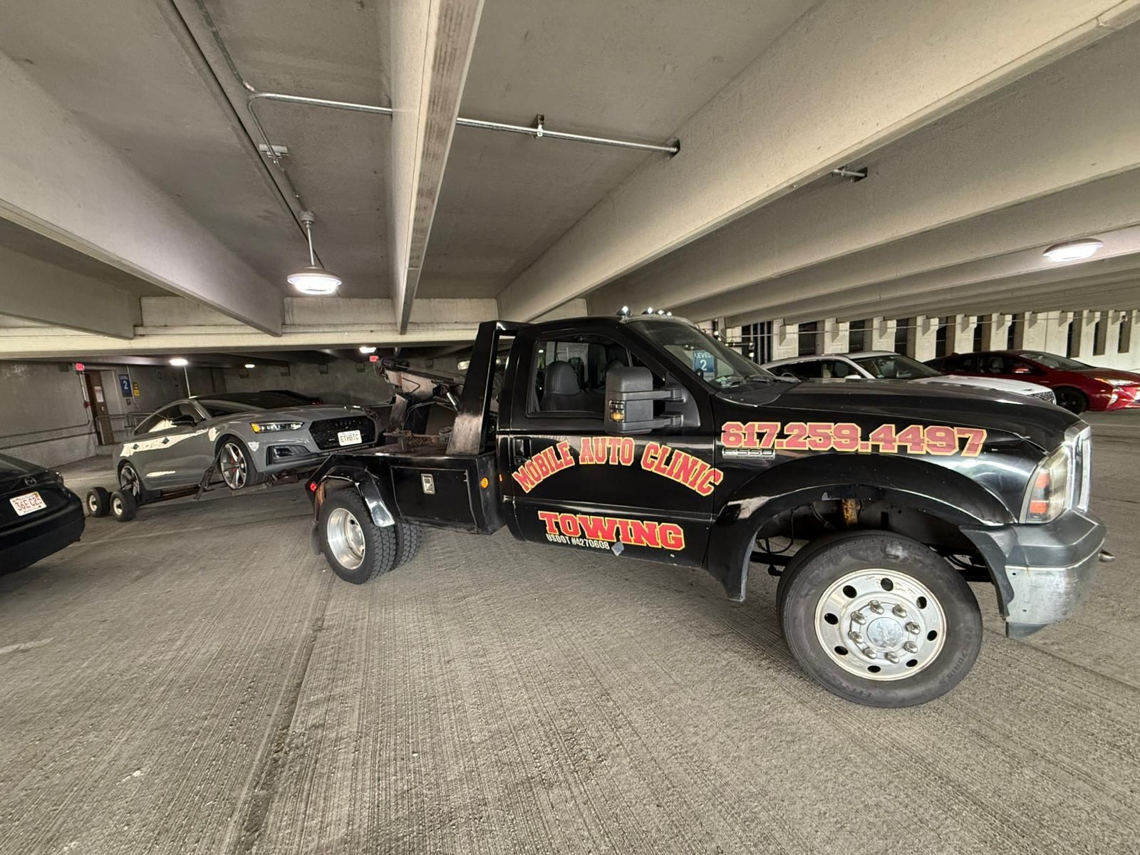 Tow truck in a parking garage towing a gray car.