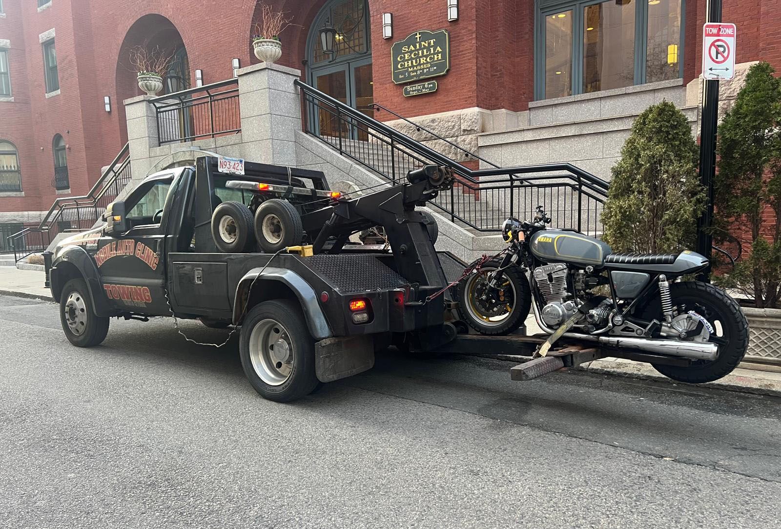 Tow truck hauling a customized motorcycle on a city street.