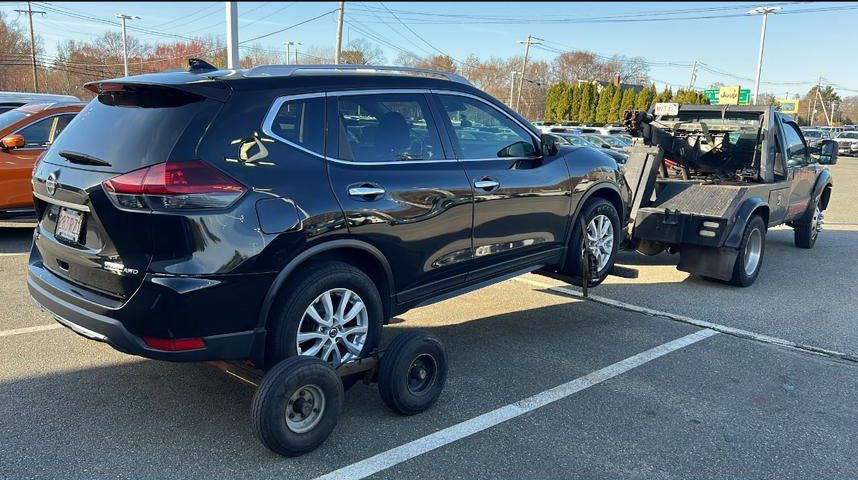 Black SUV being towed on a flatbed truck in a parking lot; wheels on the rear.