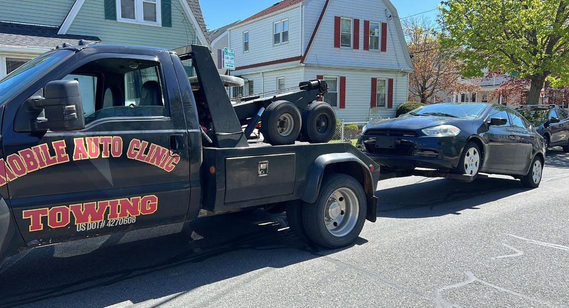 Tow truck towing a dark car on a residential street. The truck has 