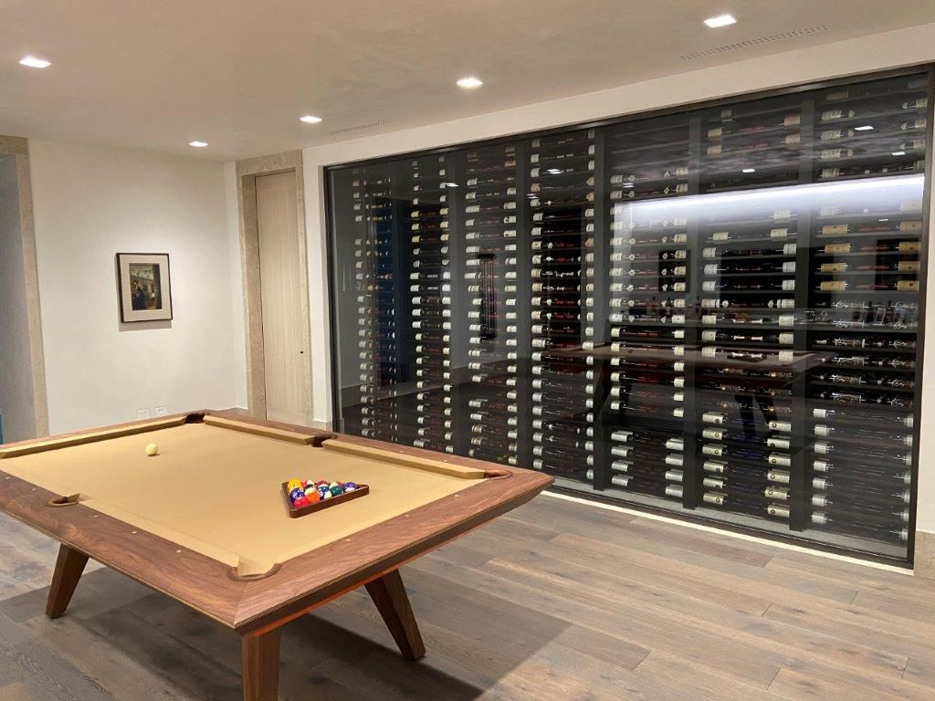 Pool table in a room with a wall of wine bottles behind a glass partition.