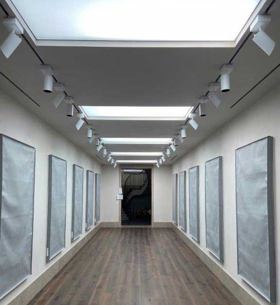 Long hallway with artworks covered in fabric; track lighting on the ceiling, wood floor.
