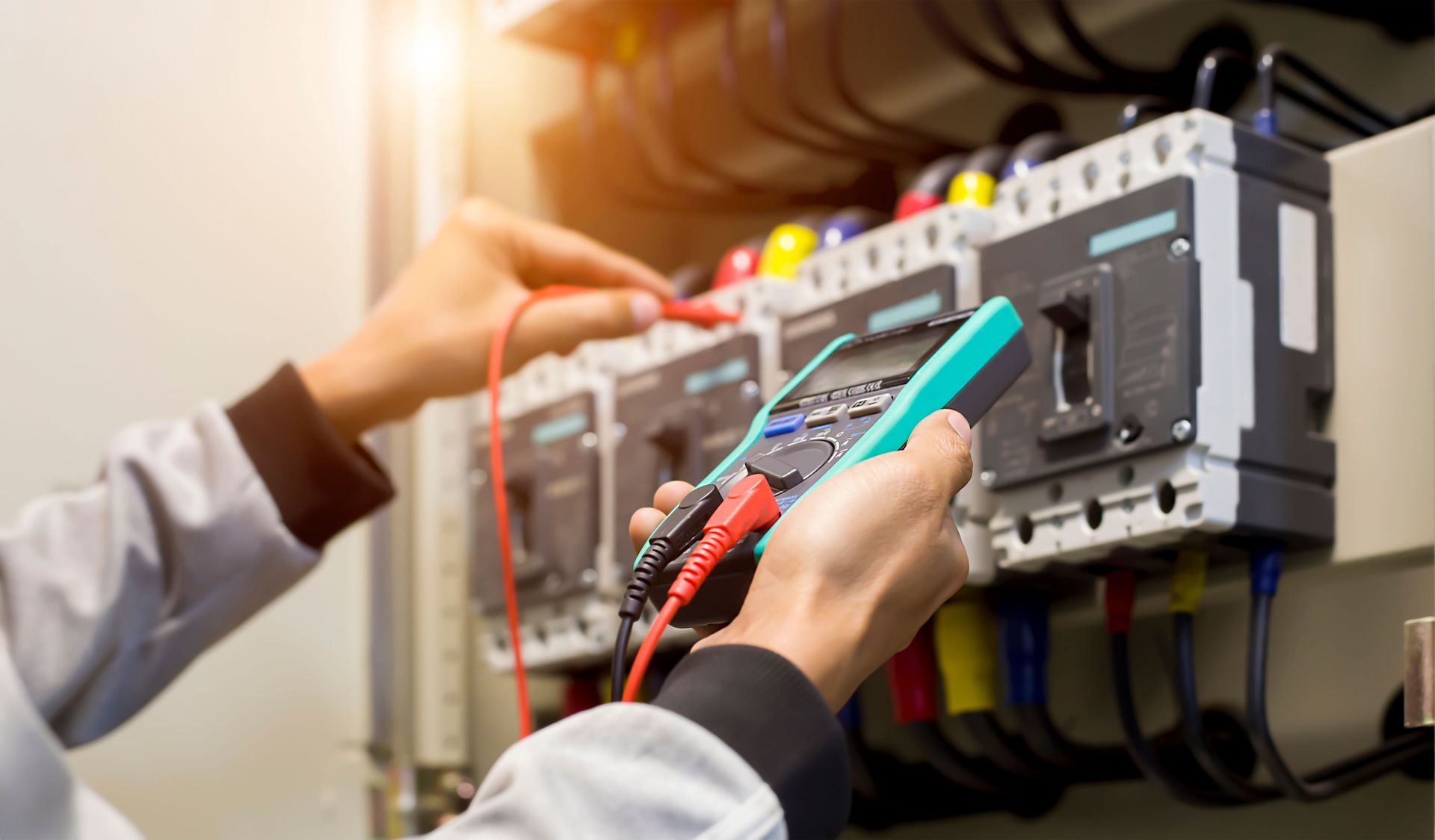 Electrician using a multimeter to test electrical panel wiring, with red and black probes.