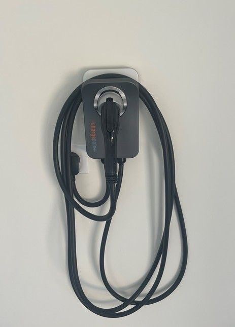 EV charger mounted on a white wall, cable coiled below.