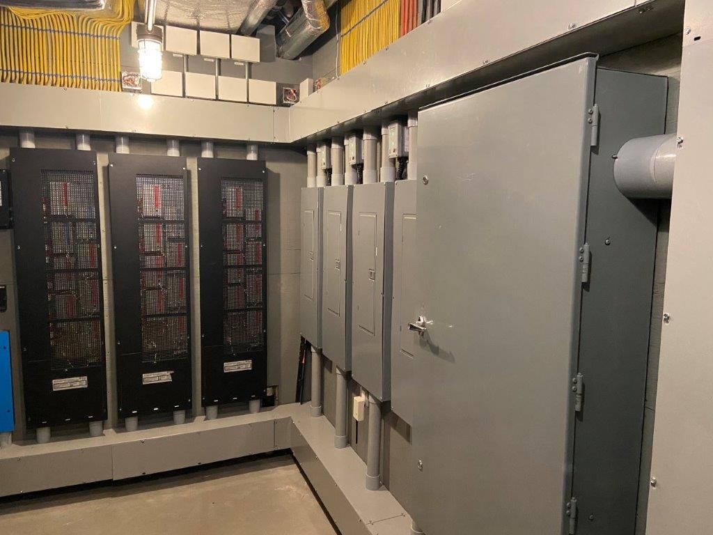 Electrical equipment room with gray panels, conduits, and ventilation, indoors.