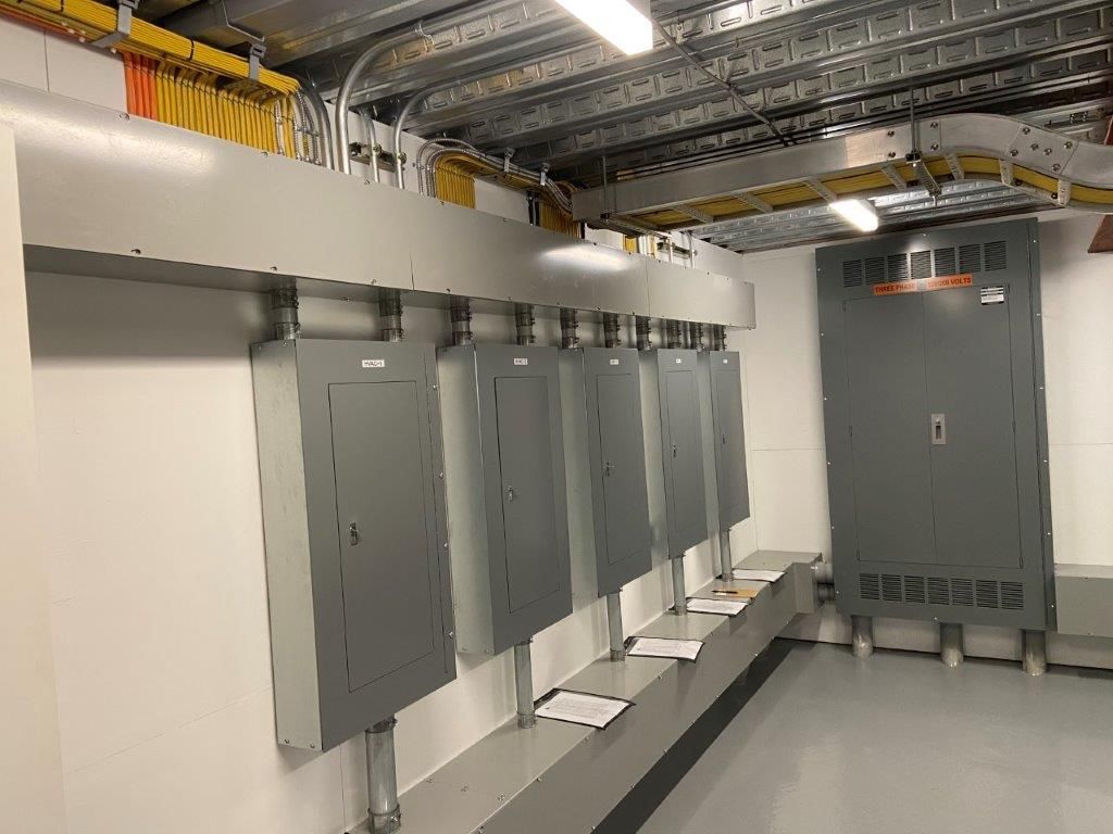 Electrical panel room with grey panels mounted on a ledge, wiring above.