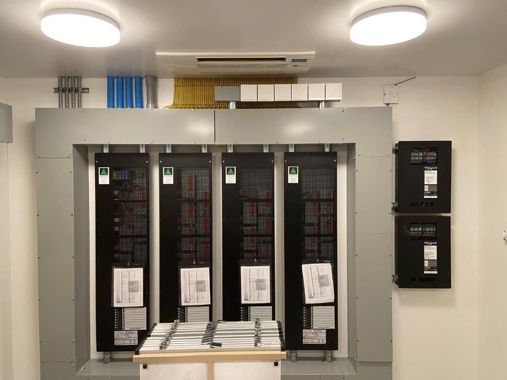 Electrical control panel room with large gray panels, paperwork, and other equipment.