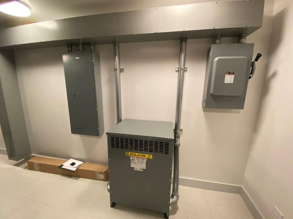 Electrical equipment mounted on a wall: transformer, two grey boxes, and conduits.
