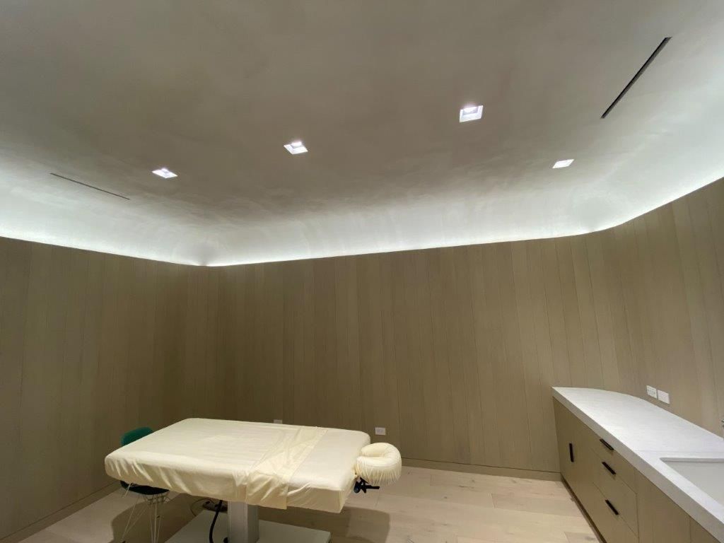 Massage room with a massage table, light wood panel walls, and recessed lighting.