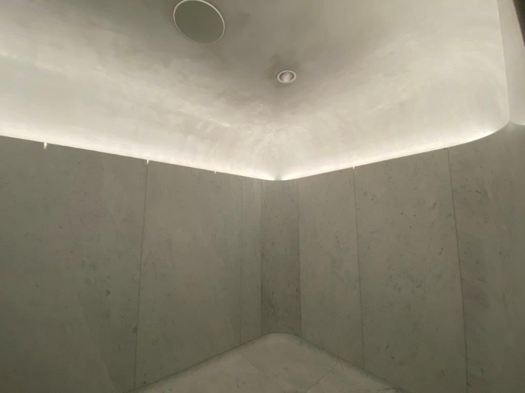 Corner of a modern, minimalist bathroom with gray marble walls, and a curved ceiling with soft lighting.