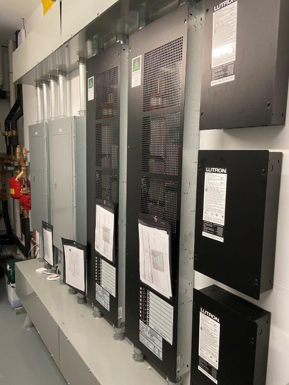 Electrical equipment in a white-walled room; metal cabinets and boxes, various sizes; ventilation grates.