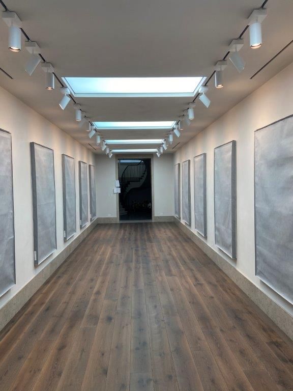 Long hallway in art gallery, wooden floor, artworks on walls, spotlights, and skylights.
