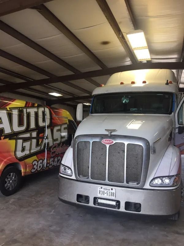 White Peterbilt semi-truck and a yellow and red Auto Glass Shop van parked in a garage.