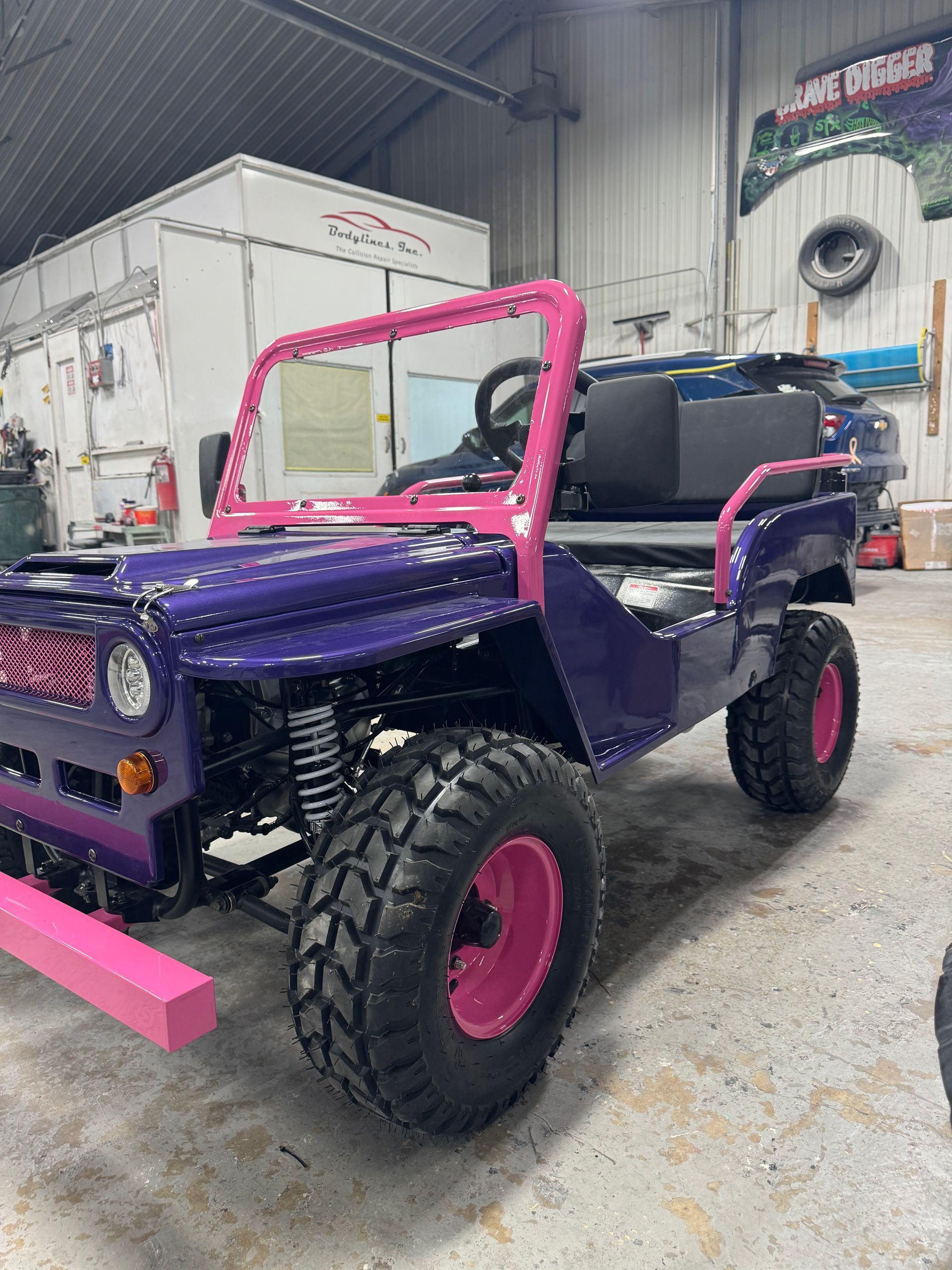 Purple off-road Jeep with pink roll cage and wheels in a garage workshop.