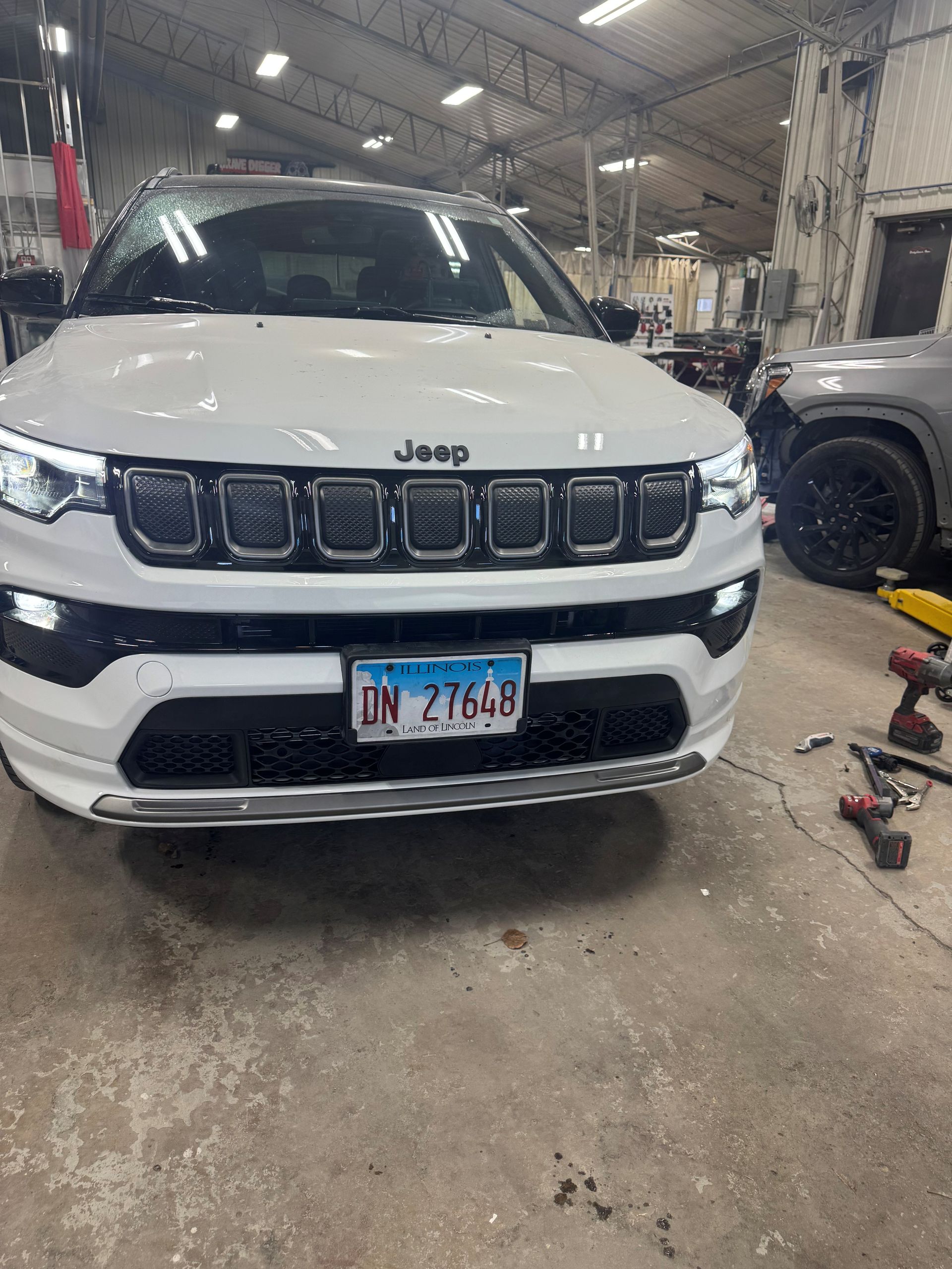 White pickup truck, rear view, in a shop, black tire, silver wheel, black bed cover, and red tail light - After