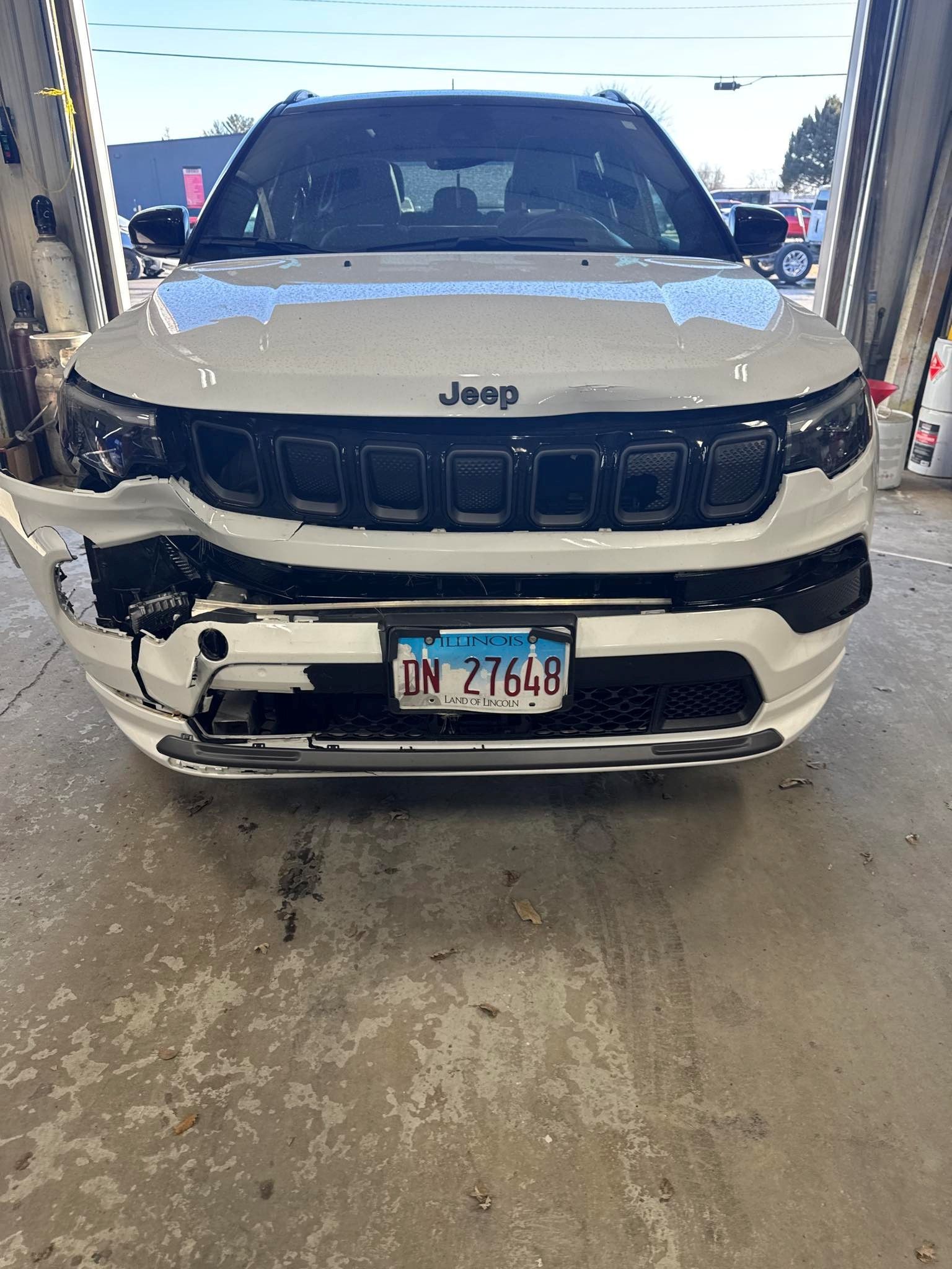 White pickup truck, rear view, in a shop, black tire, silver wheel, black bed cover, and red tail light - before