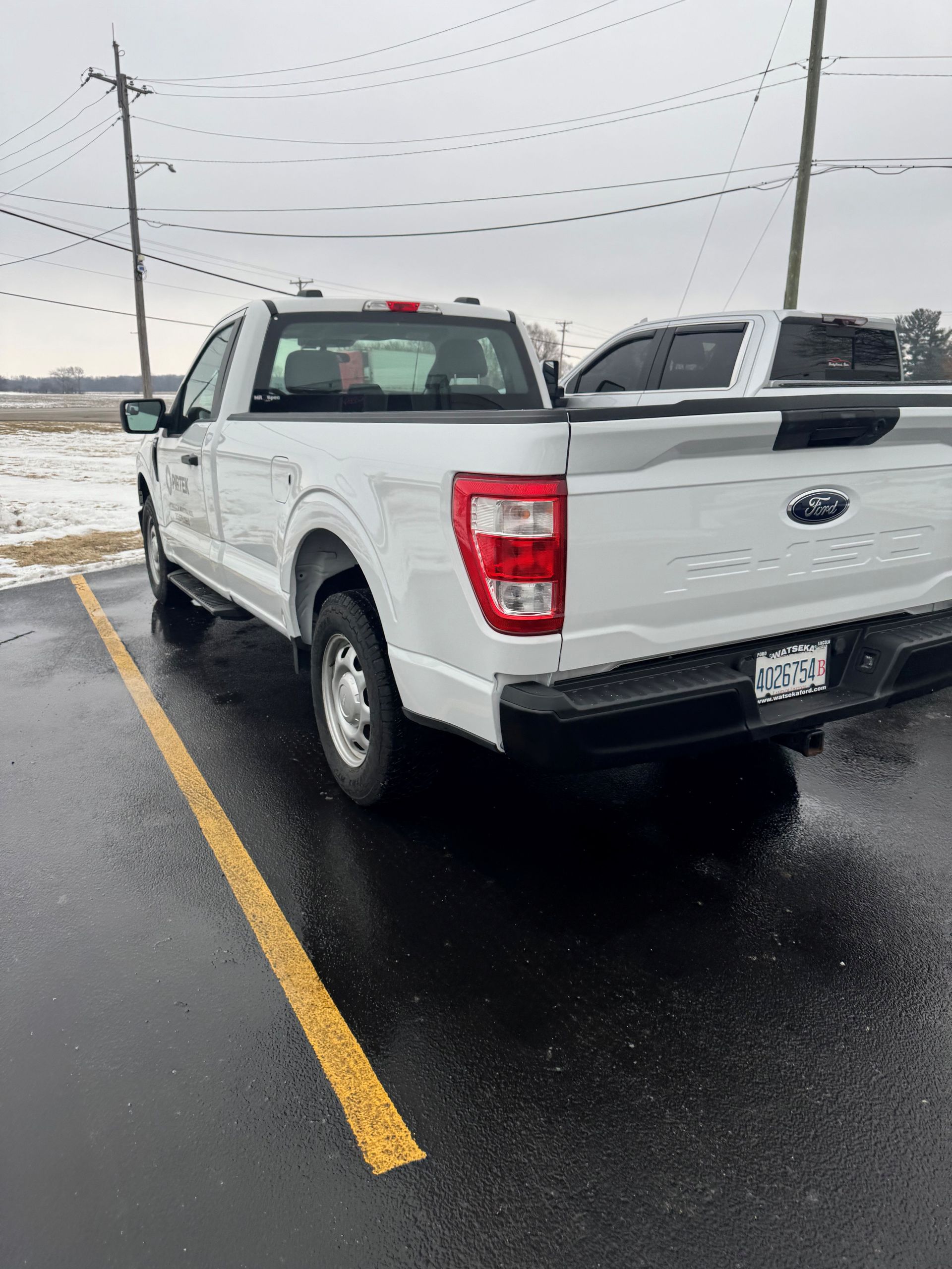 White pickup truck, rear view, in a shop, black tire, silver wheel, black bed cover, and red tail light - After