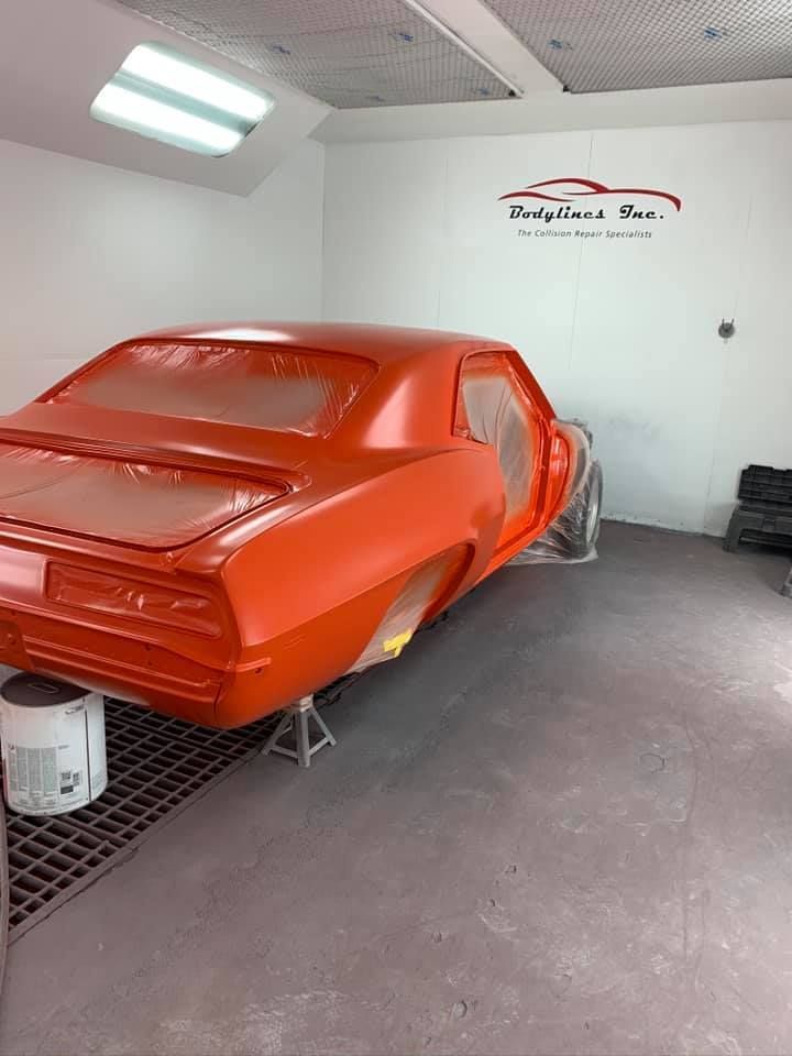 Orange classic car in a paint booth being restored.