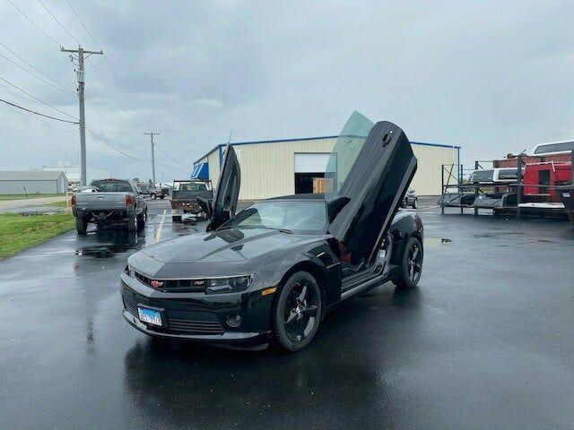 Black Chevrolet Camaro with doors open, parked on wet pavement in front of a building.