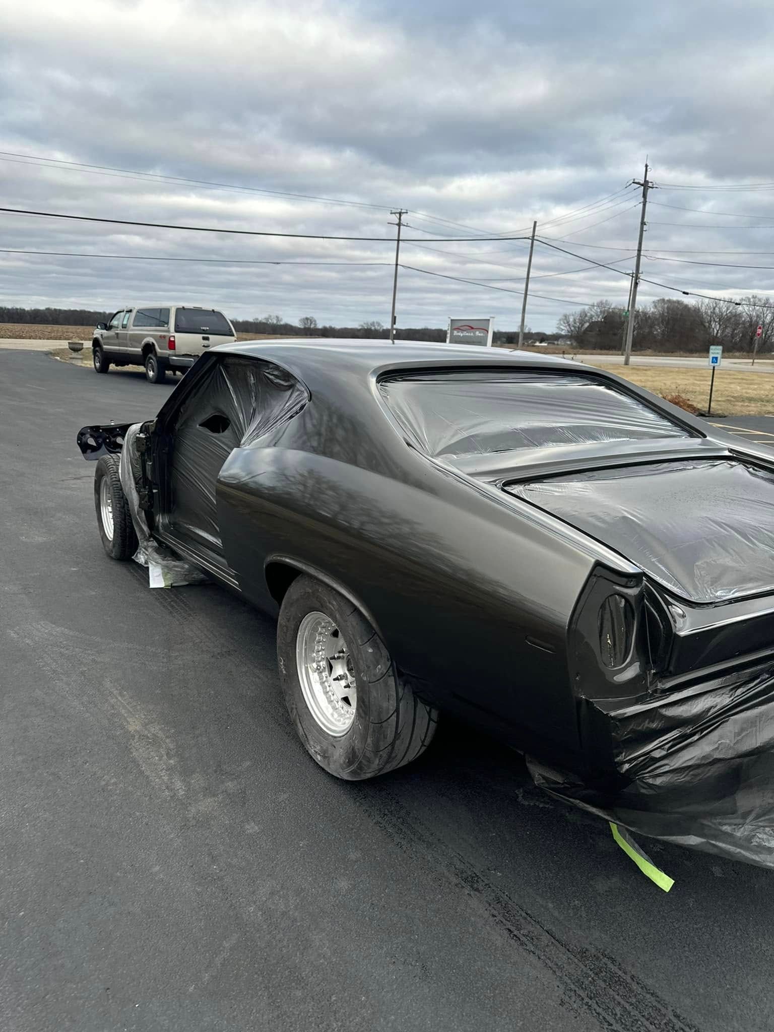 Black classic car with wide tires, parked on asphalt, cloudy sky.