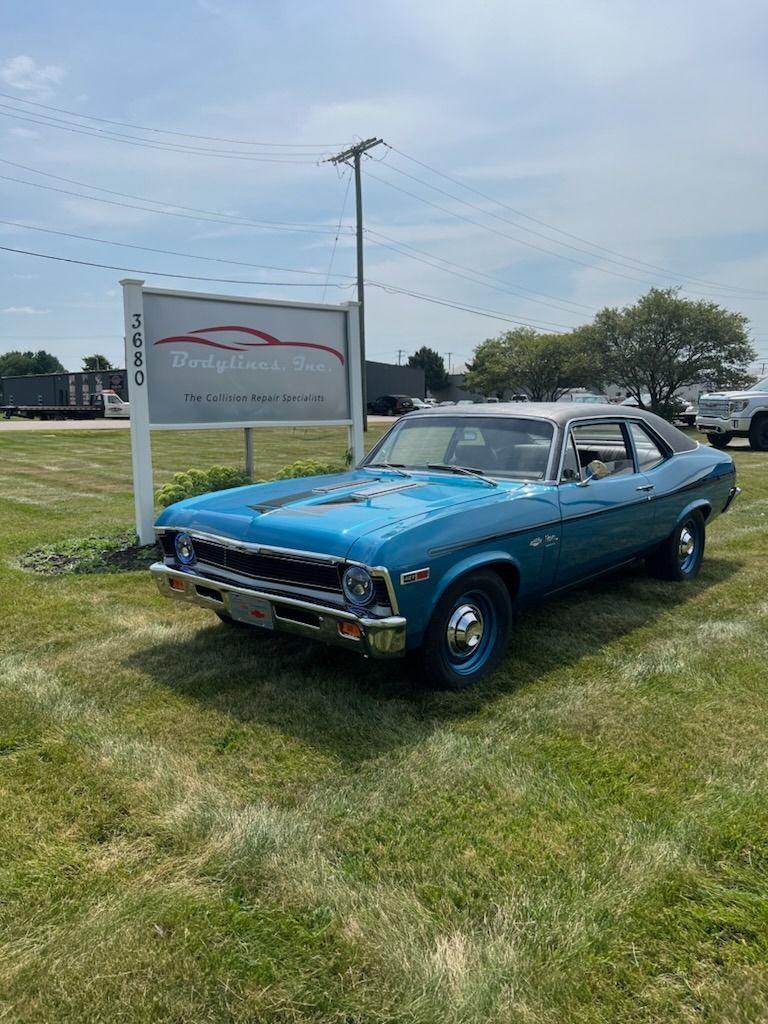 Blue classic car parked in front of a sign, sunny day.
