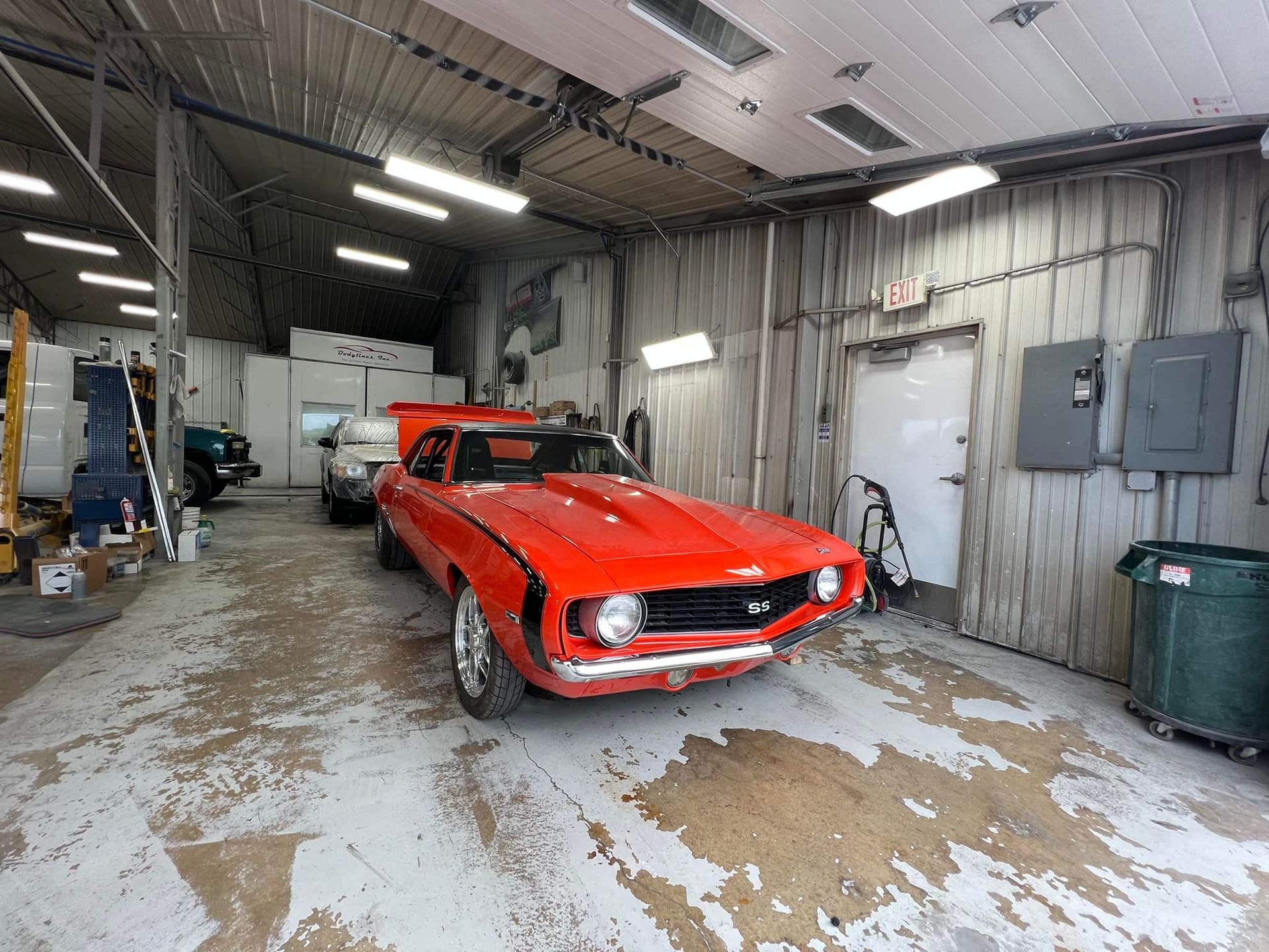 Red classic car inside a garage, with white walls and a messy floor.