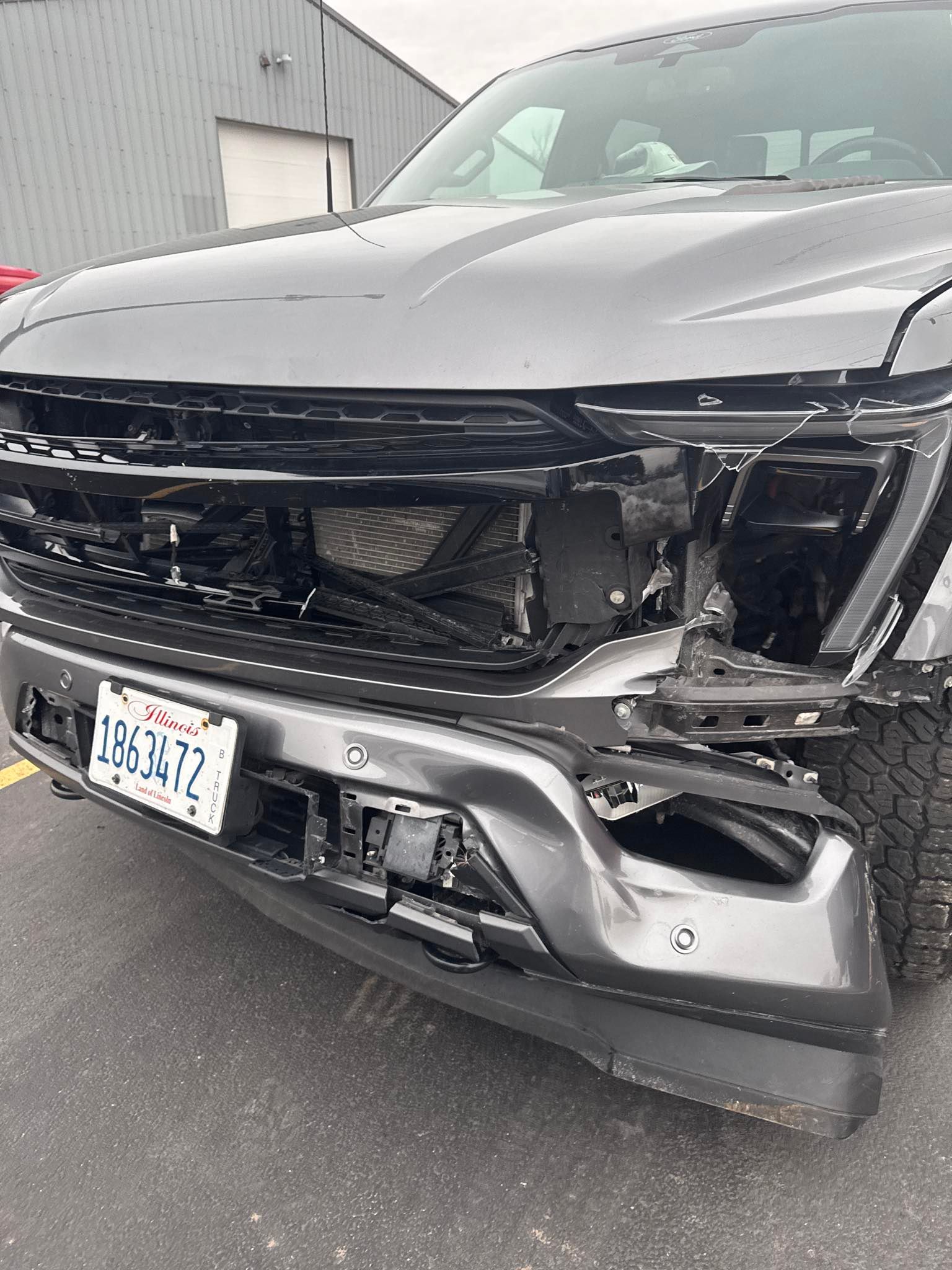 White pickup truck, rear view, in a shop, black tire, silver wheel, black bed cover, and red tail light - before