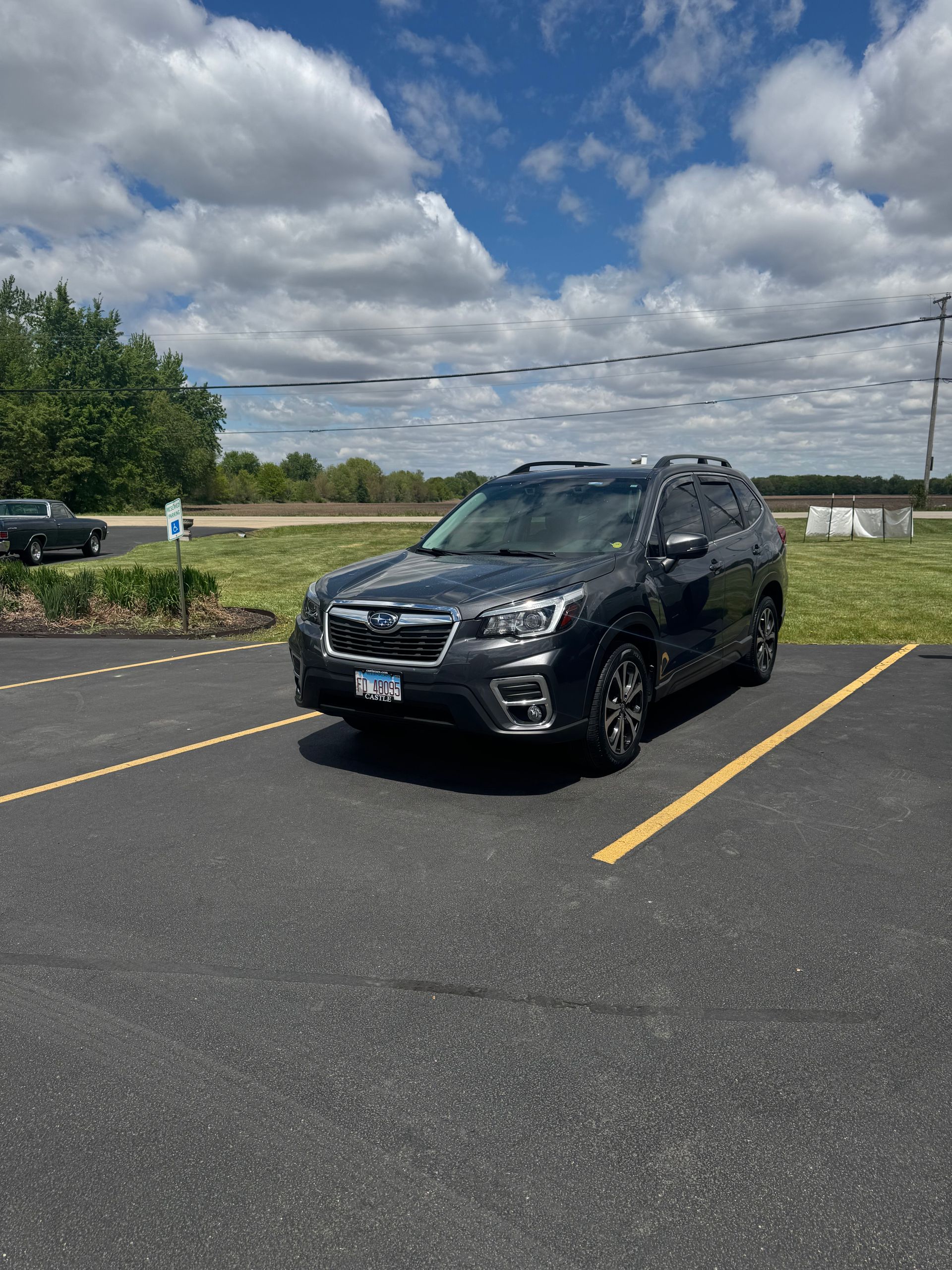 Black SUV parked in a lot under a cloudy sky, centered between yellow lines.