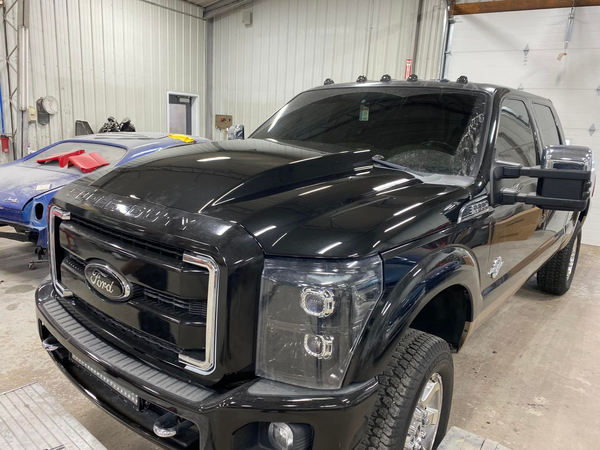 Black Ford truck inside a garage; car bodywork in the background.