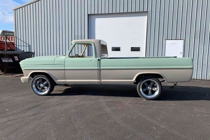Mint and beige classic Ford pickup truck parked in front of a gray building with a closed garage door.