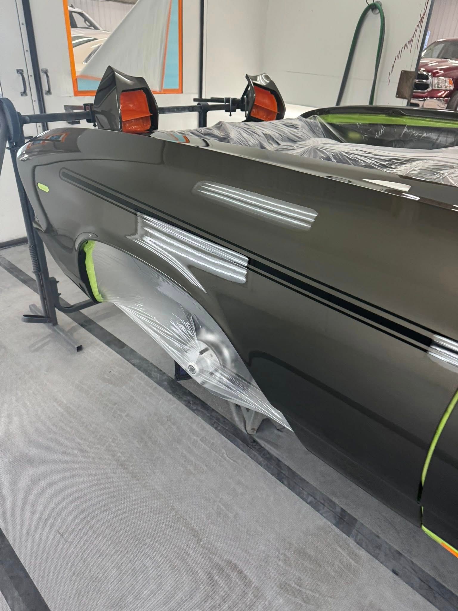 Car body panel being worked on in a workshop; grey with black stripe, masking tape applied.
