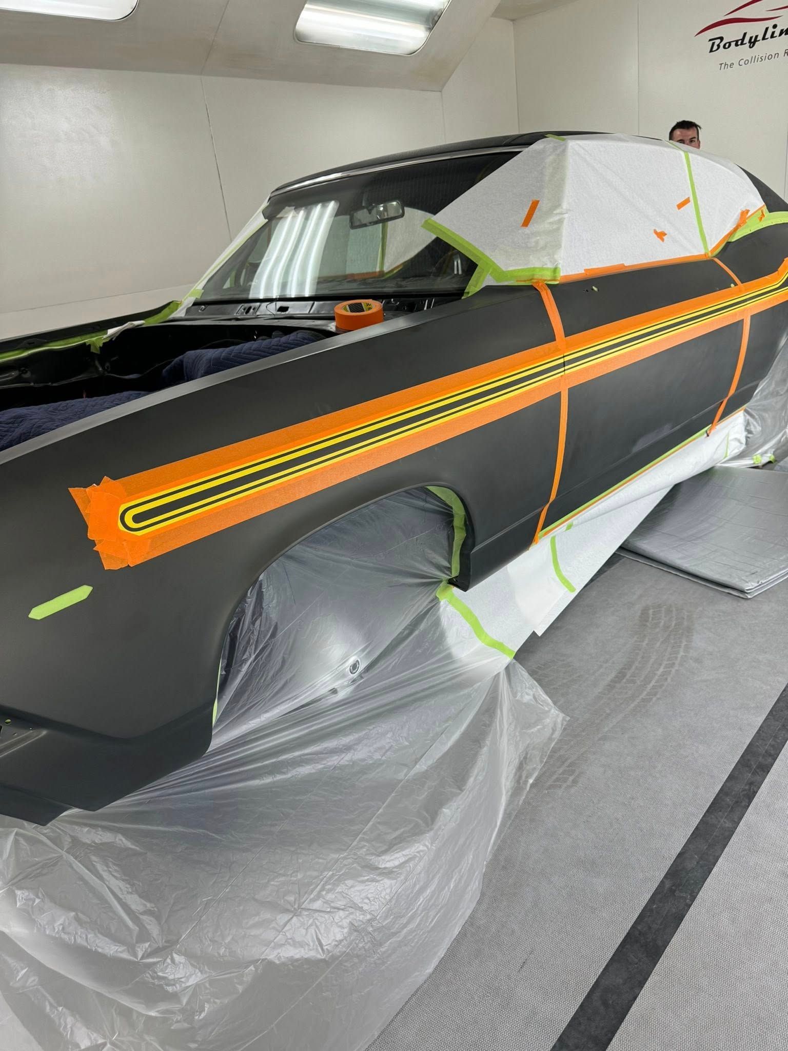 Car masked for painting with black body and orange stripe in a workshop.