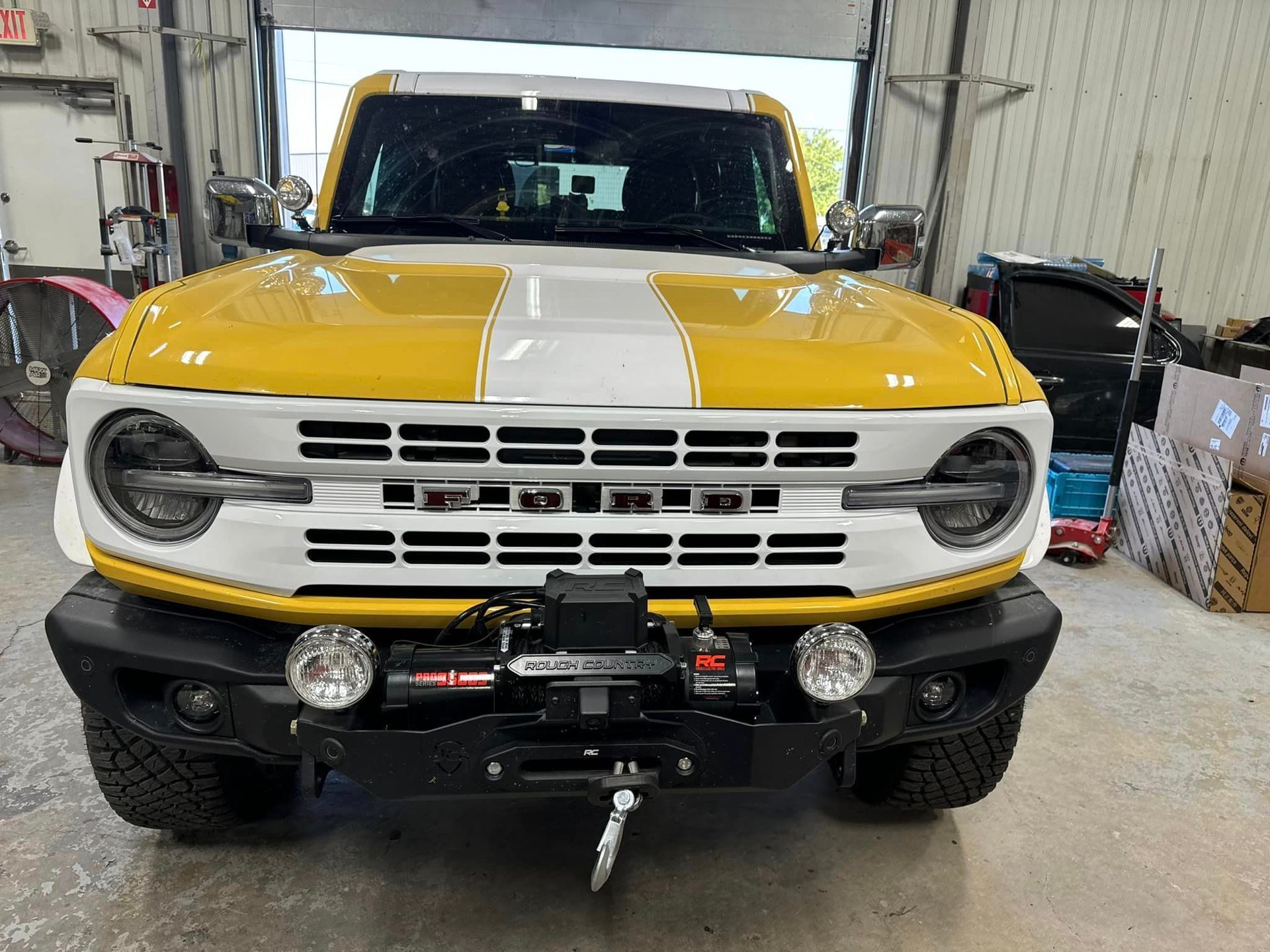 Yellow and white Ford Bronco, front view, with winch, auxiliary lights, and racing stripes.