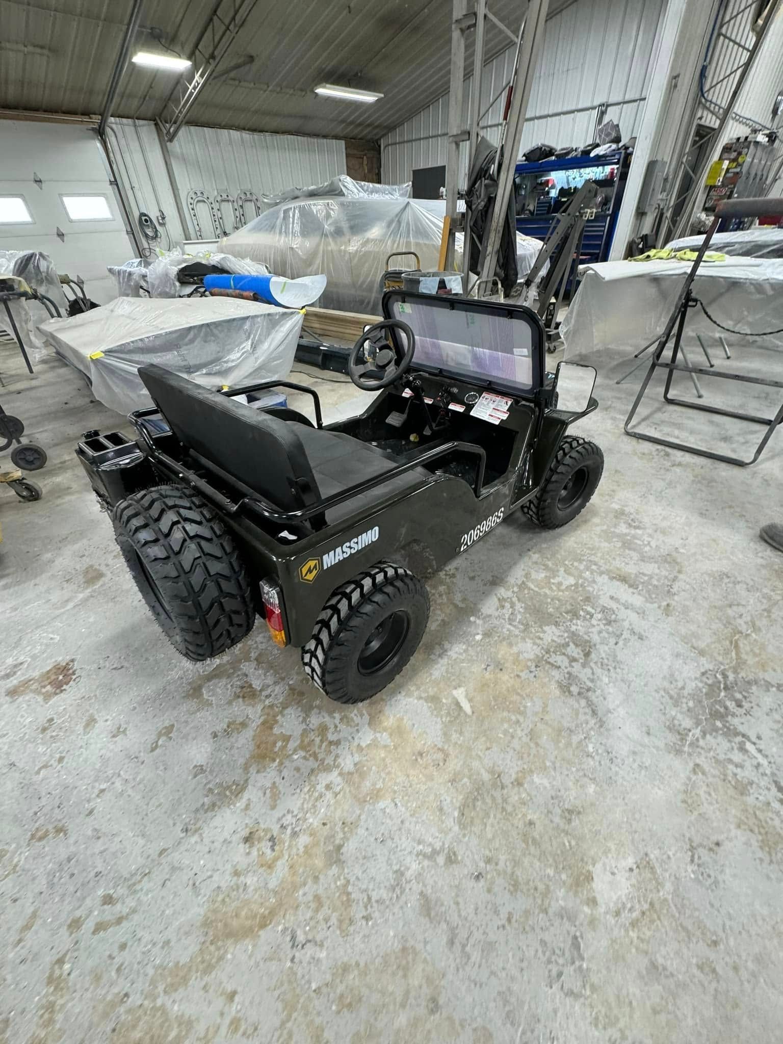 Black mini-Jeep with off-road tires, a spare tire, and roll bar inside a workshop.
