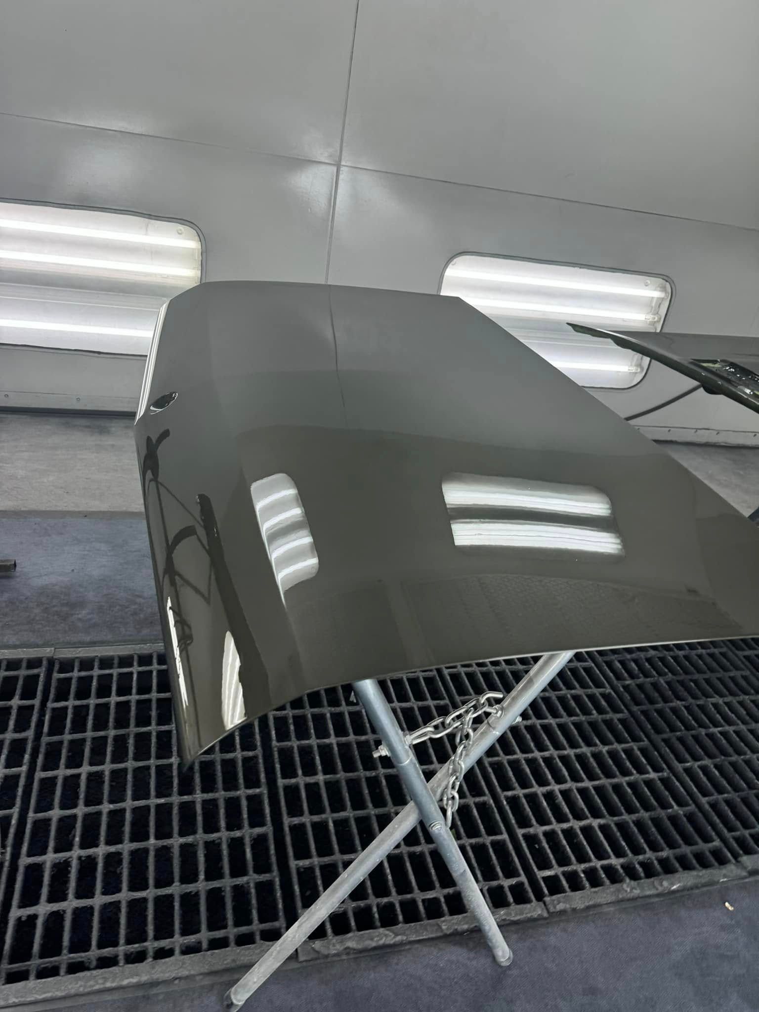 A car hood, recently painted, is drying in a paint booth.  Reflections of overhead lights are visible.