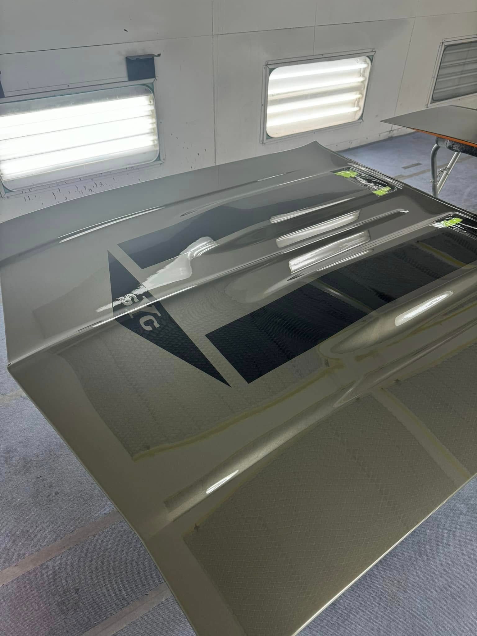 Car hood with custom green and black paint job in a workshop, under fluorescent lights.