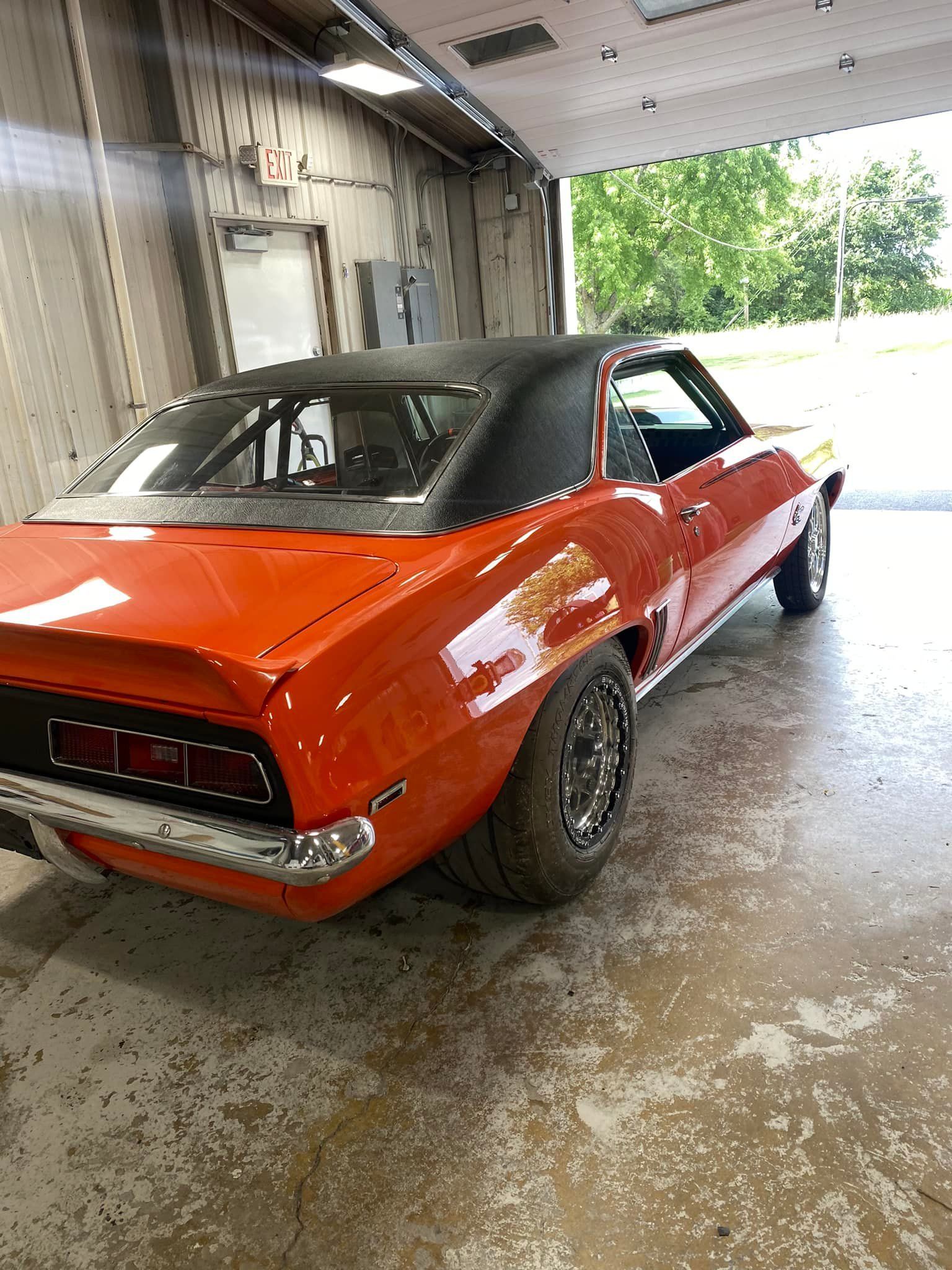 Orange and black classic car in a garage with large tires.