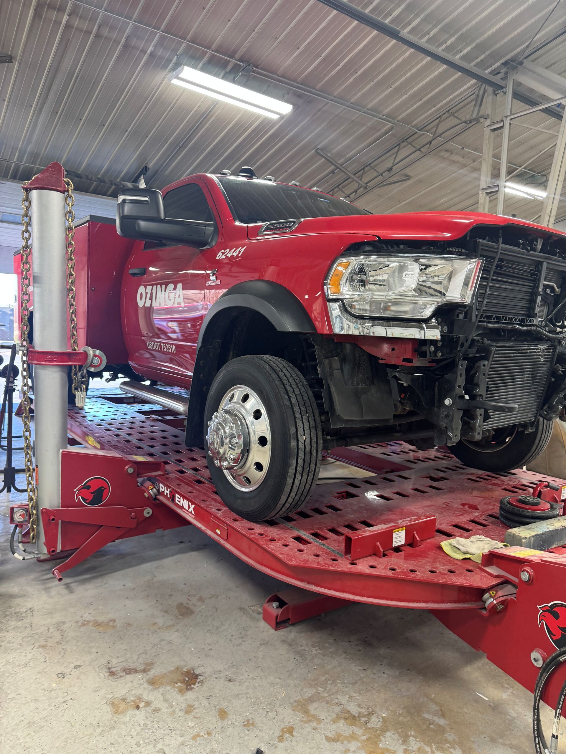 Red pickup truck on an auto lift in a garage, front end partially disassembled.