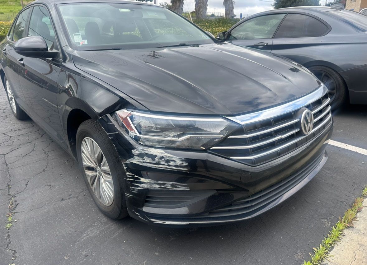 A black volkswagen jetta is parked in a parking lot next to another car.