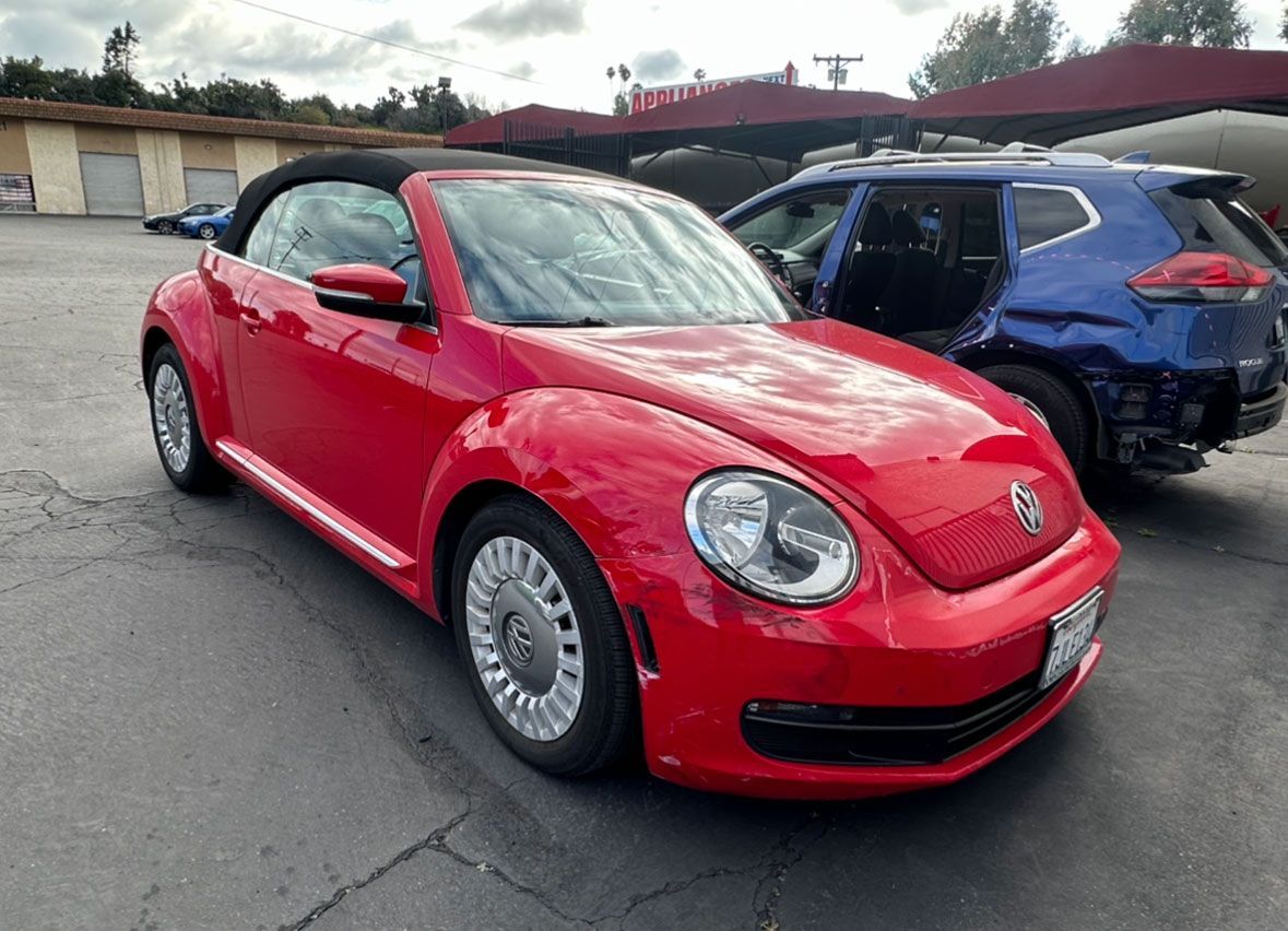 A red volkswagen beetle convertible is parked next to a blue suv in a parking lot.