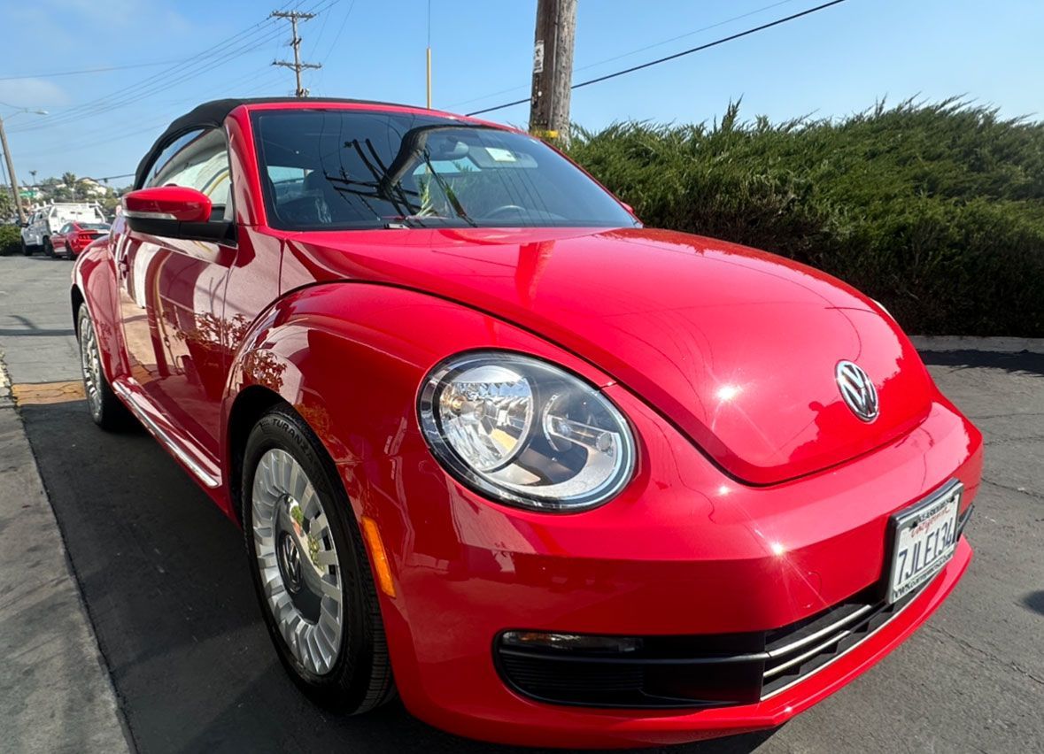 A red volkswagen beetle convertible is parked in a parking lot.