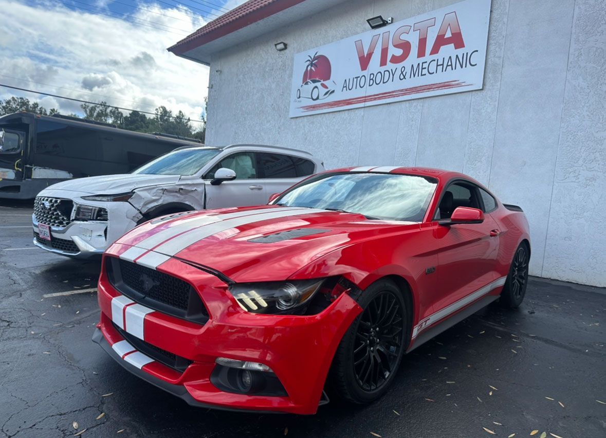 A red mustang is parked in front of a car dealership.