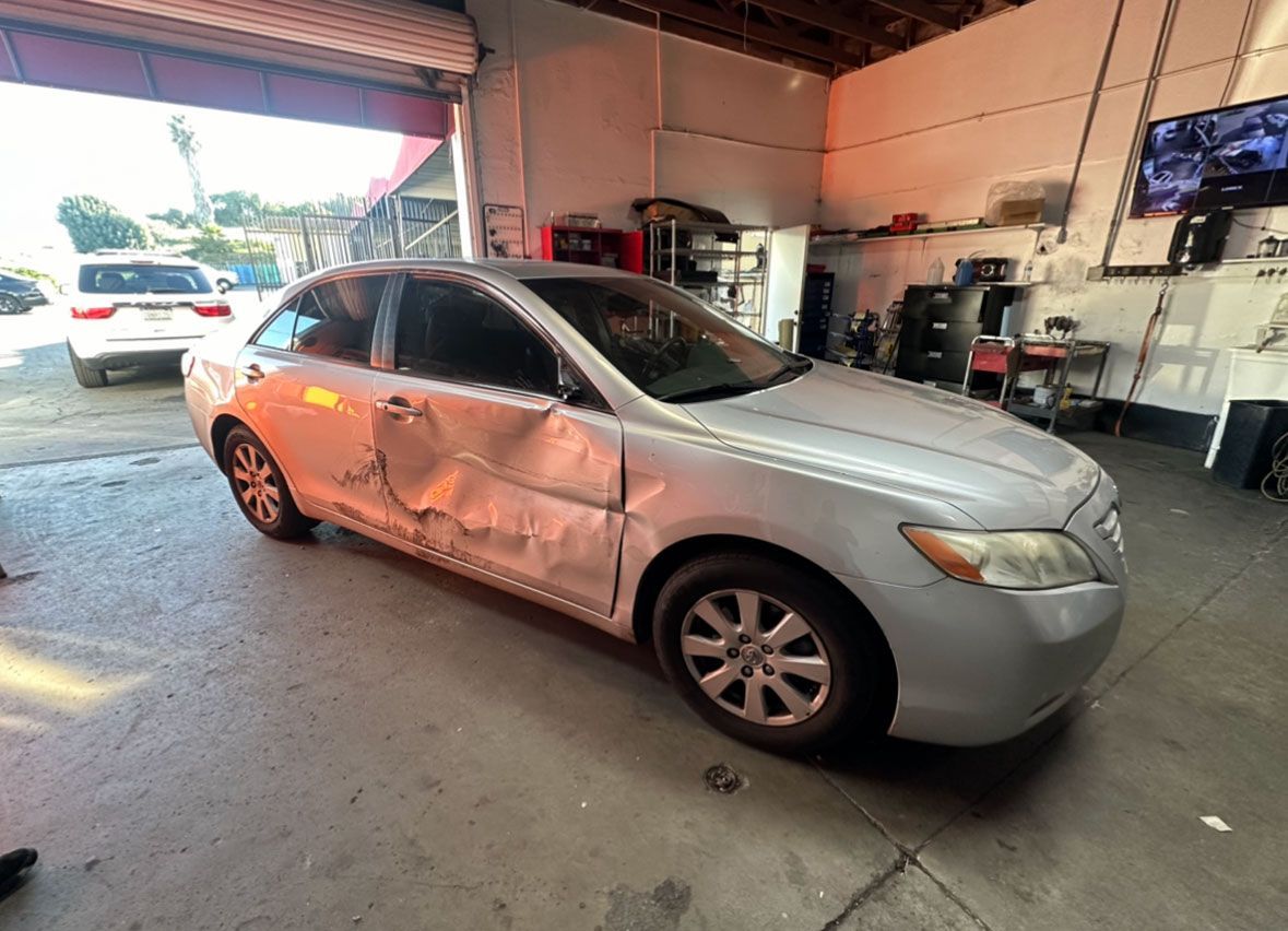 A silver car with a damaged side is parked in a garage.