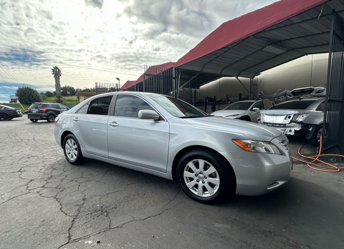 A silver car is parked under a tent in a parking lot.