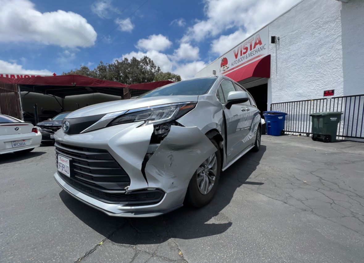 A silver car with a damaged front end is parked in front of a building.
