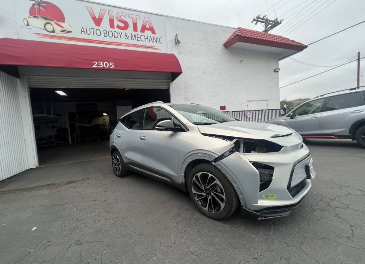 A silver car is parked in front of a vista auto body shop.